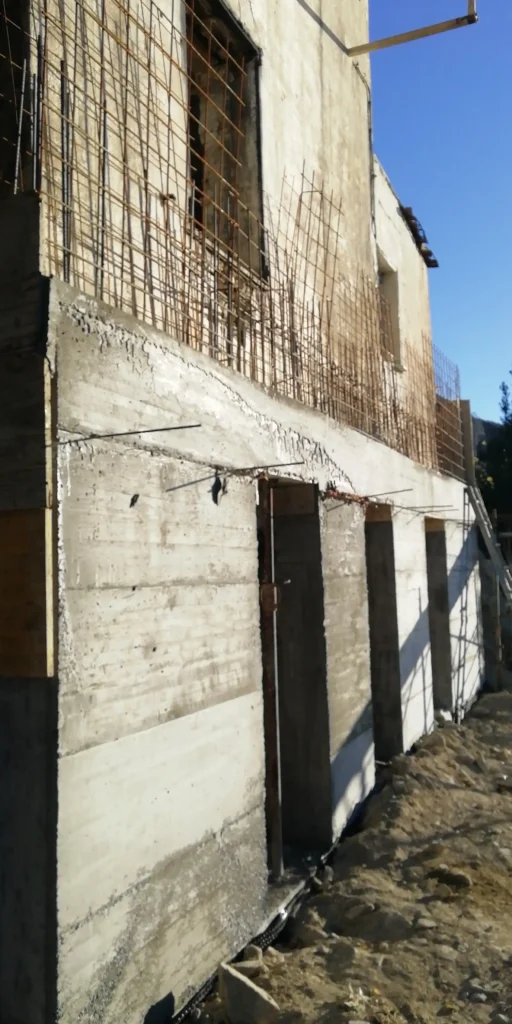 Nuove fondamenta in cemento armato con ferri a vista in un cantiere a Mentone, a sostegno di un edificio esistente. Il contrasto tra la vecchia struttura e le nuove opere di consolidamento è evidente. L'immagine illustra l'importanza delle opere di sottofondazione per la stabilità e la sicurezza sismica degli immobili in Costa Azzurra.