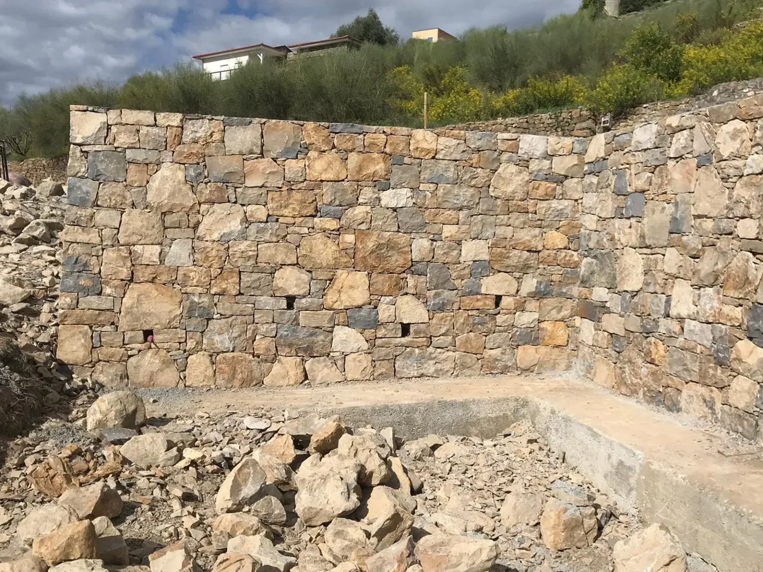 Muro di contenimento in pietra faccia vista completato, con terreno scavato retrostante, cantiere villa a Vallebona, Costa Azzurra. Impresa edile.