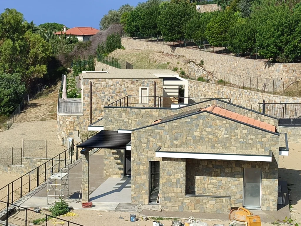 Villa in costruzione con rivestimento in pietra naturale e design moderno, immersa nel verde a Bordighera.